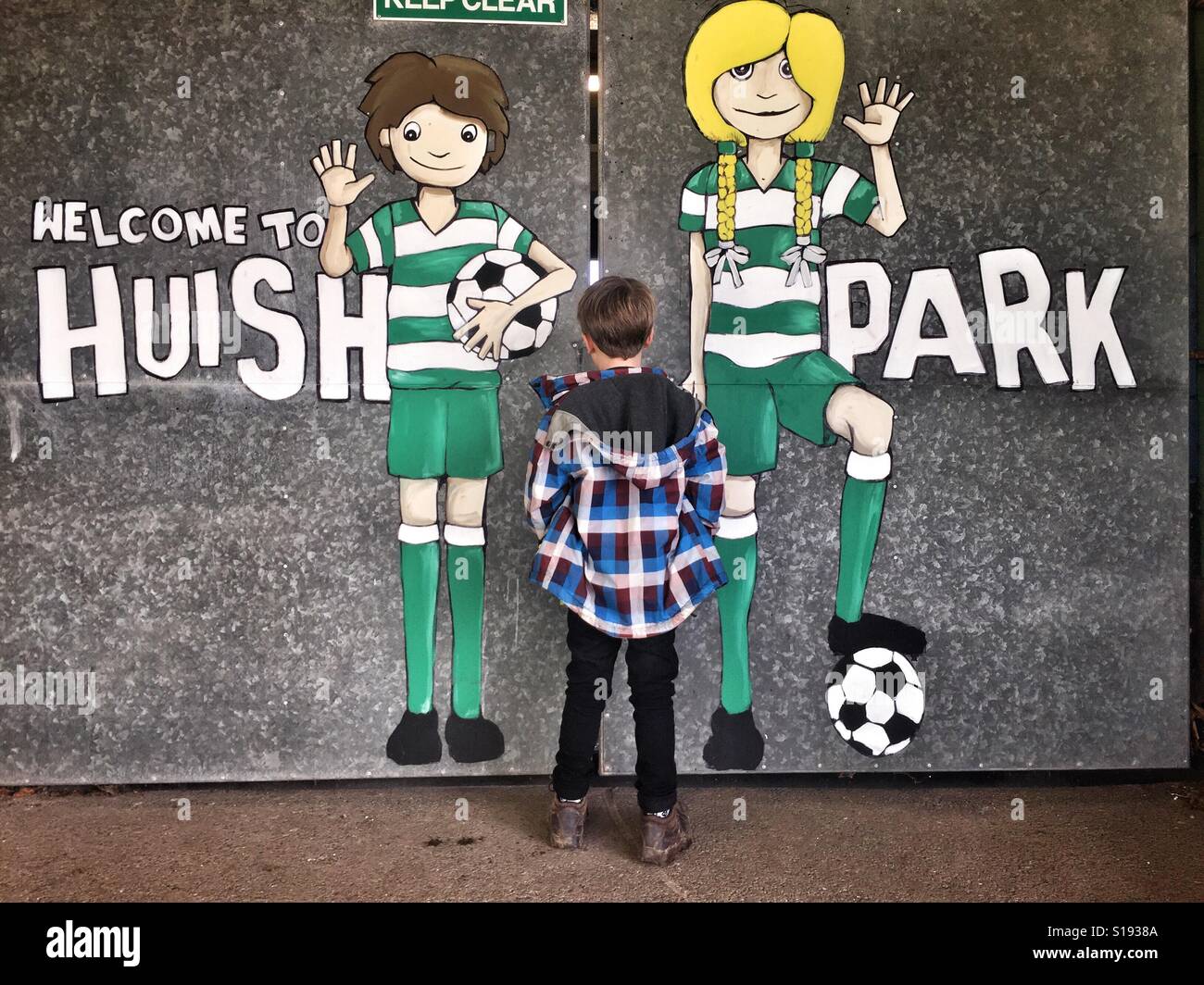 Un jeune garçon se profile au une lacune dans les portes avant d'un match de football à Yeovil Football Club à Huish Park dans le Somerset. Banque D'Images