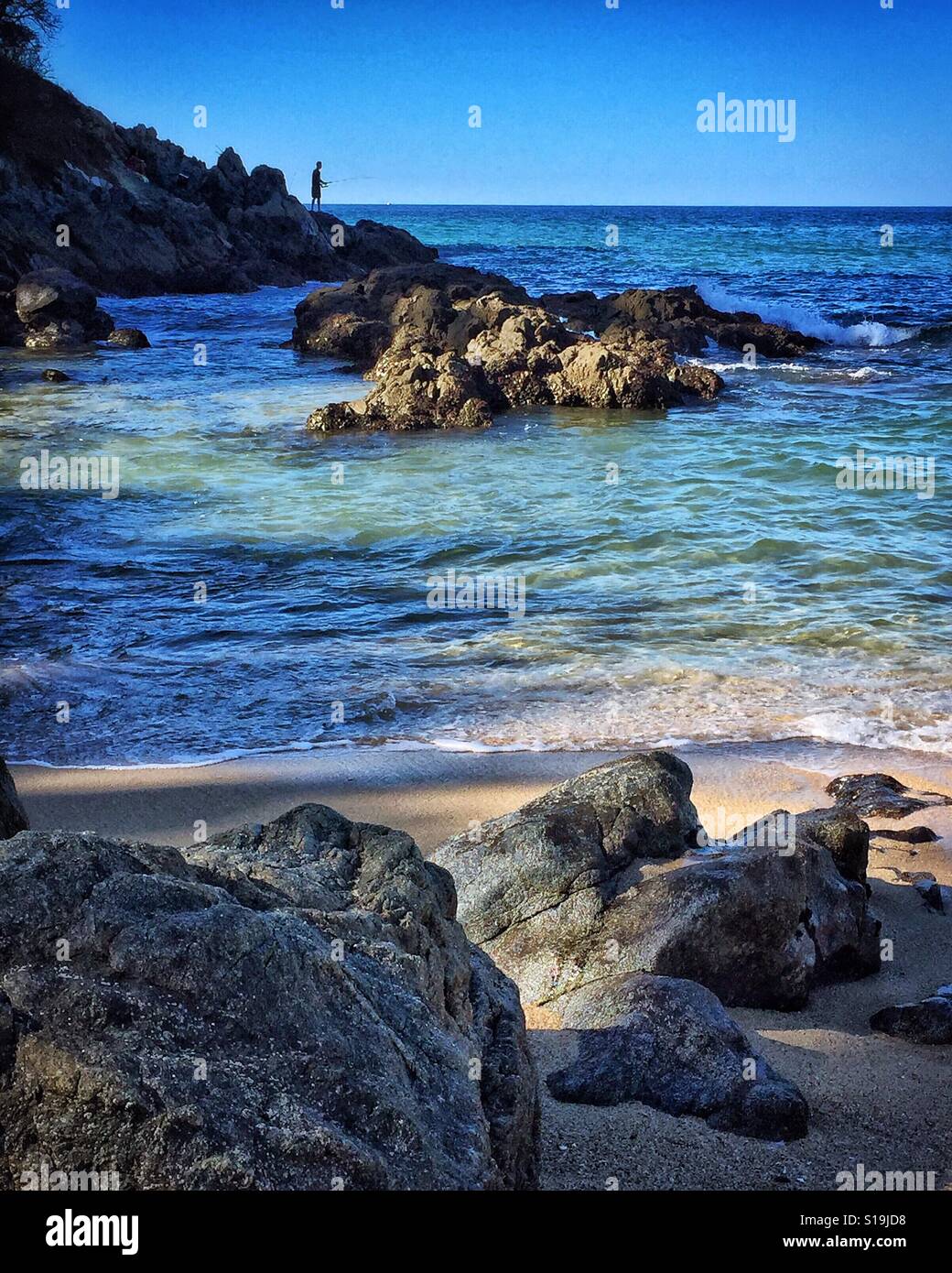 Au loin un homme se tient sur le rocky point la pêche sur ce rude et belle section d'une plage dans la Riviera Nayarit. Banque D'Images