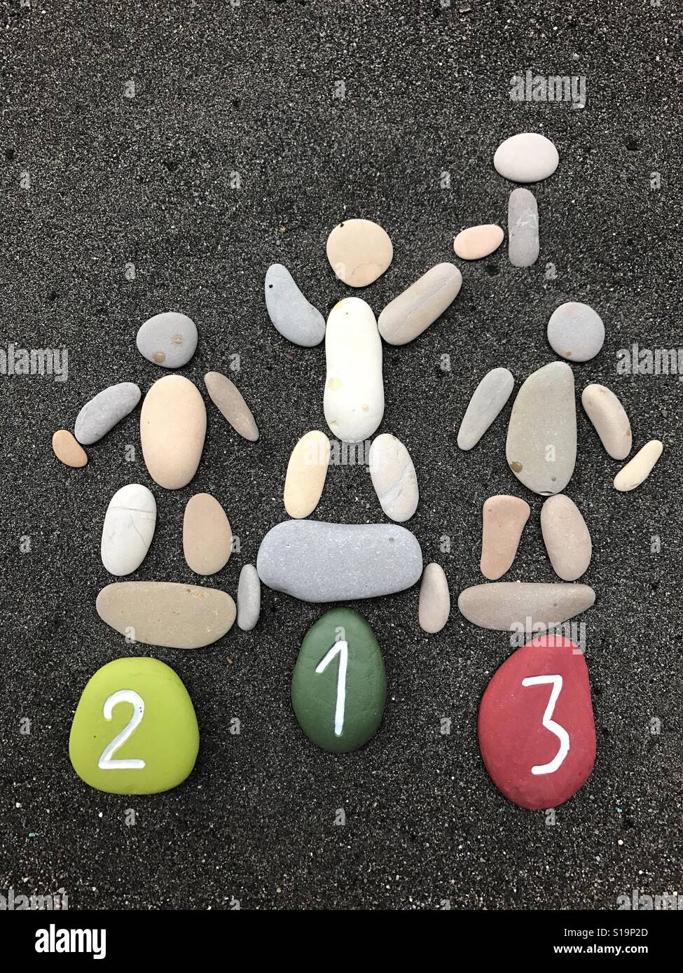 Le gagnant, composition conceptuelle avec des cailloux et des pierres sur sable volcanique noir, première, deuxième et troisième place Banque D'Images