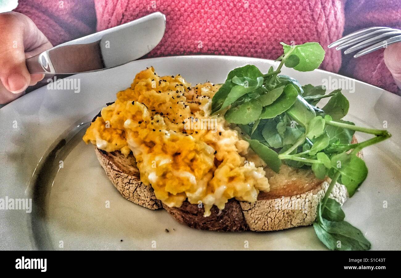 Le petit déjeuner ! Oeufs brouillés sur toast, femme et prêt à manger, avec couteau et fourchette en mains. Banque D'Images