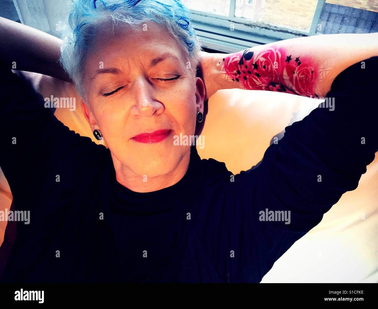 Hauts femme avec les cheveux gris et bleu et de peinture de l'avant-bras Floral tattoo relaxing at home - Image de stock capturée avec un smartphone