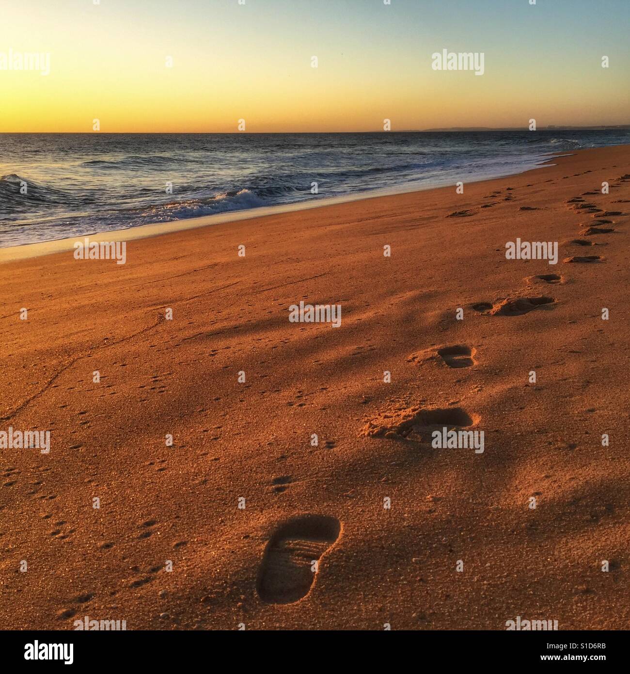 Coucher du soleil sur une plage au Portugal avec empreintes de pieds dans le sable de premier plan à l'horizon. Banque D'Images