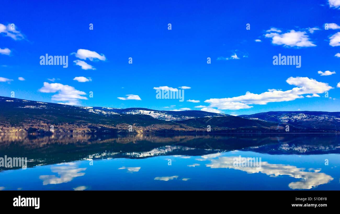 Ciel bleu, les nuages blancs et les montagnes se reflétant dans les eaux calmes du lac. Paysage. - Image de stock capturée avec un smartphone