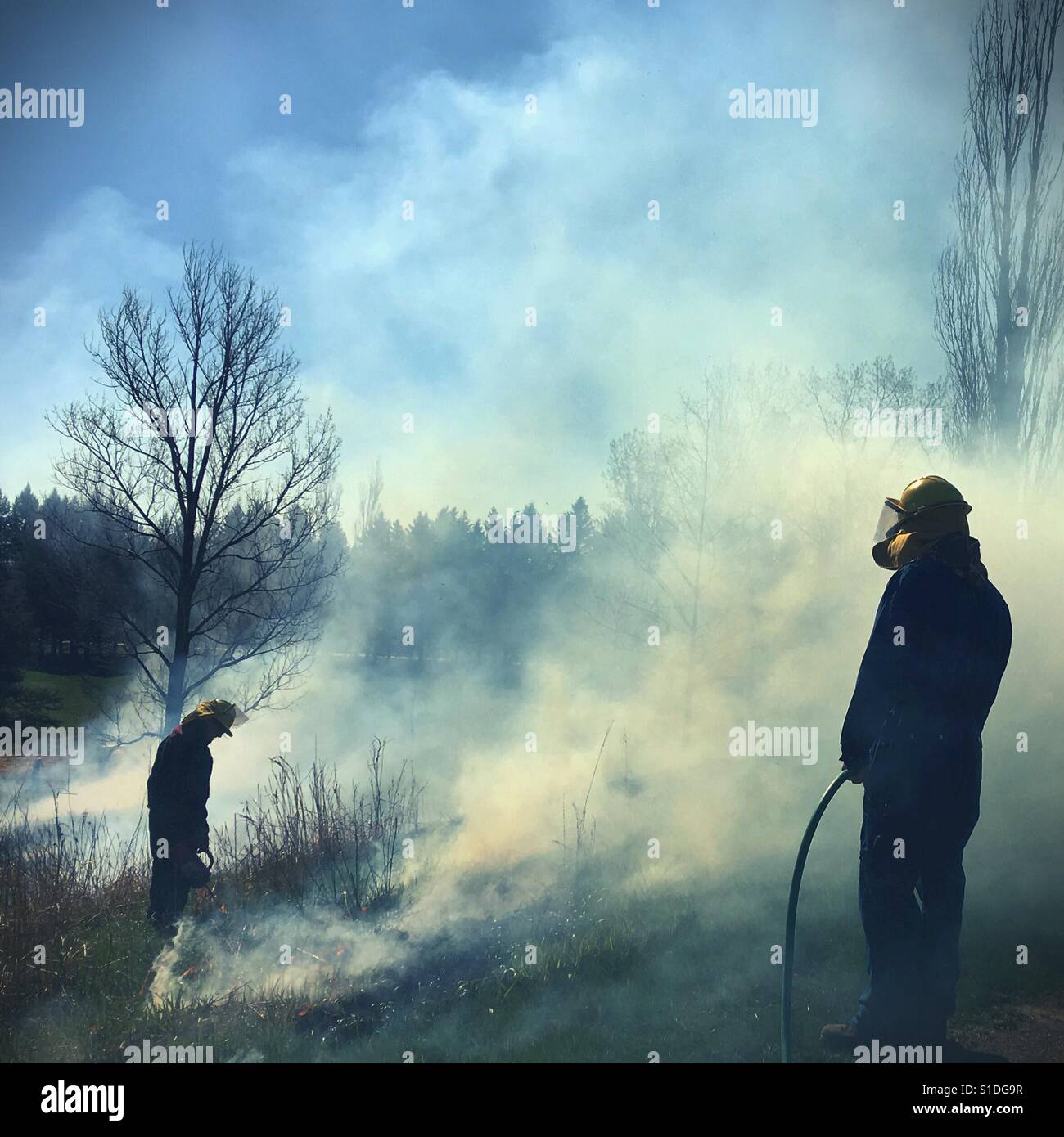 Deux personnes dans les vêtements de sécurité faisant un brûlage contrôlé d'un champ dans le Minnesota, USA. Banque D'Images
