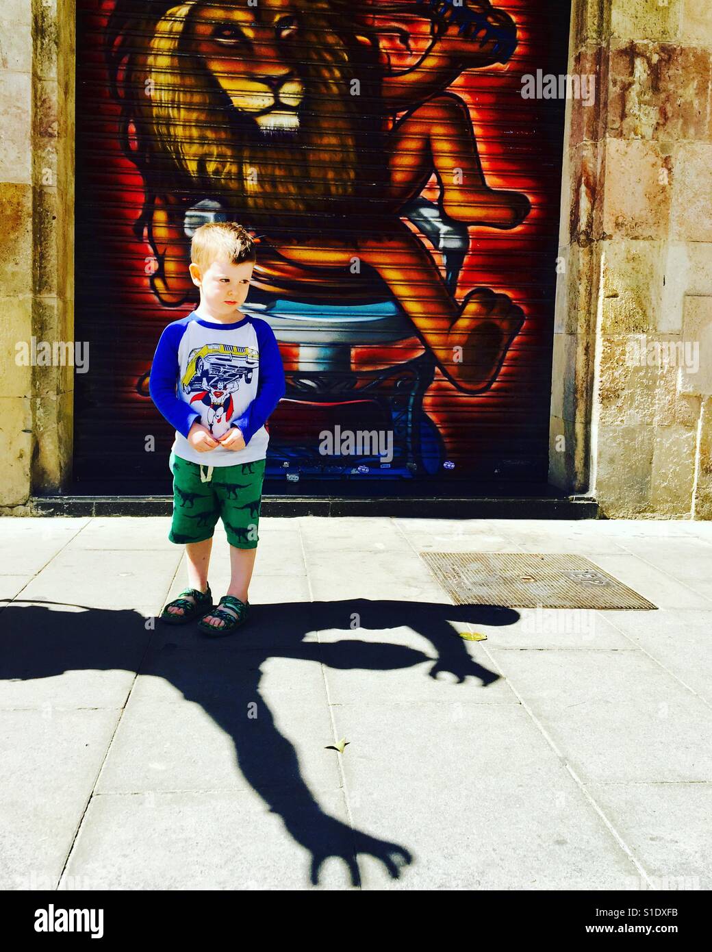 Un garçon de deux ans semble effrayé par une apparente monster ombre sur le plancher, lion style graffiti shop shutter en arrière-plan Banque D'Images