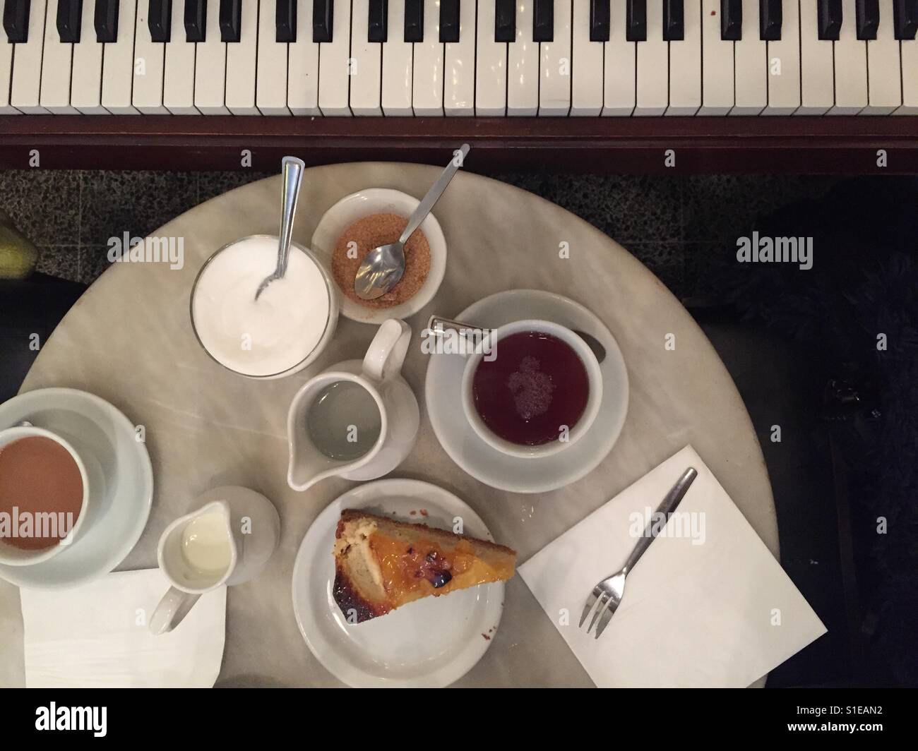 Tasses de thé et des pots de thé avec une tranche de gâteau sur une table de marbre à côté d'un piano d'un birds eye view Banque D'Images