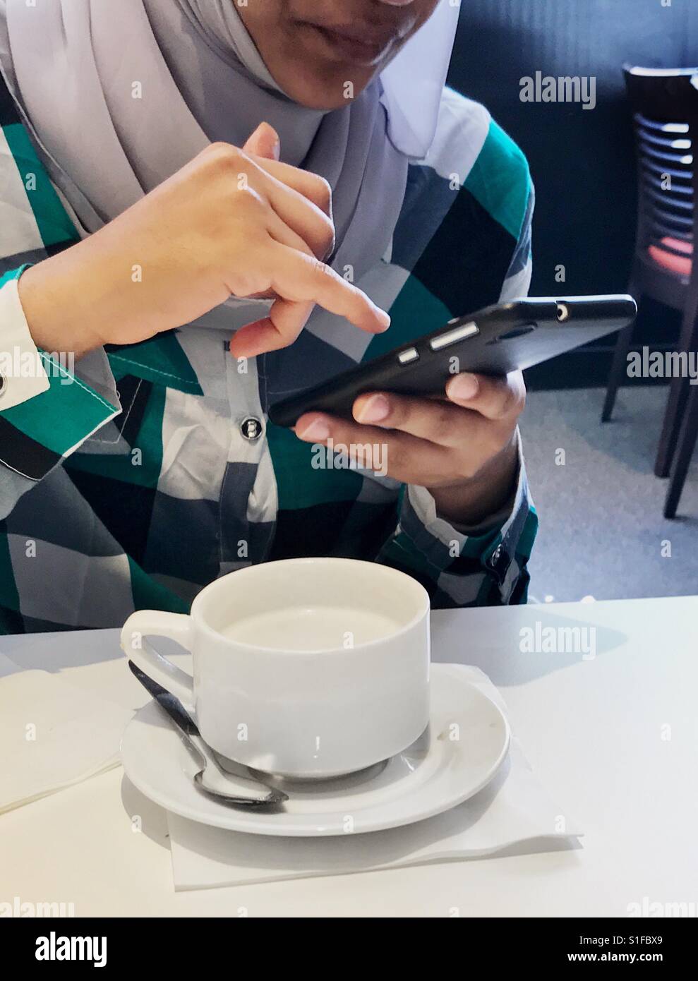 Thé du matin ; une jeune fille musulmane avec smart phone de boire du thé blanc - Image de stock capturée avec un smartphone
