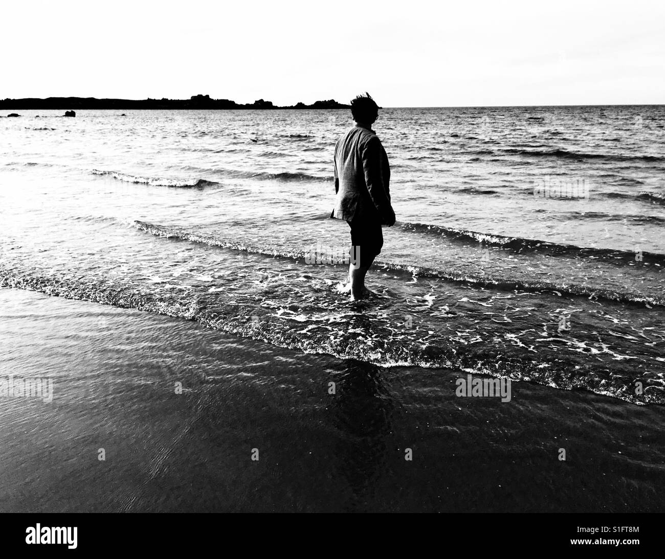 Homme marchant à travers l'eau de mer sur une plage Banque D'Images