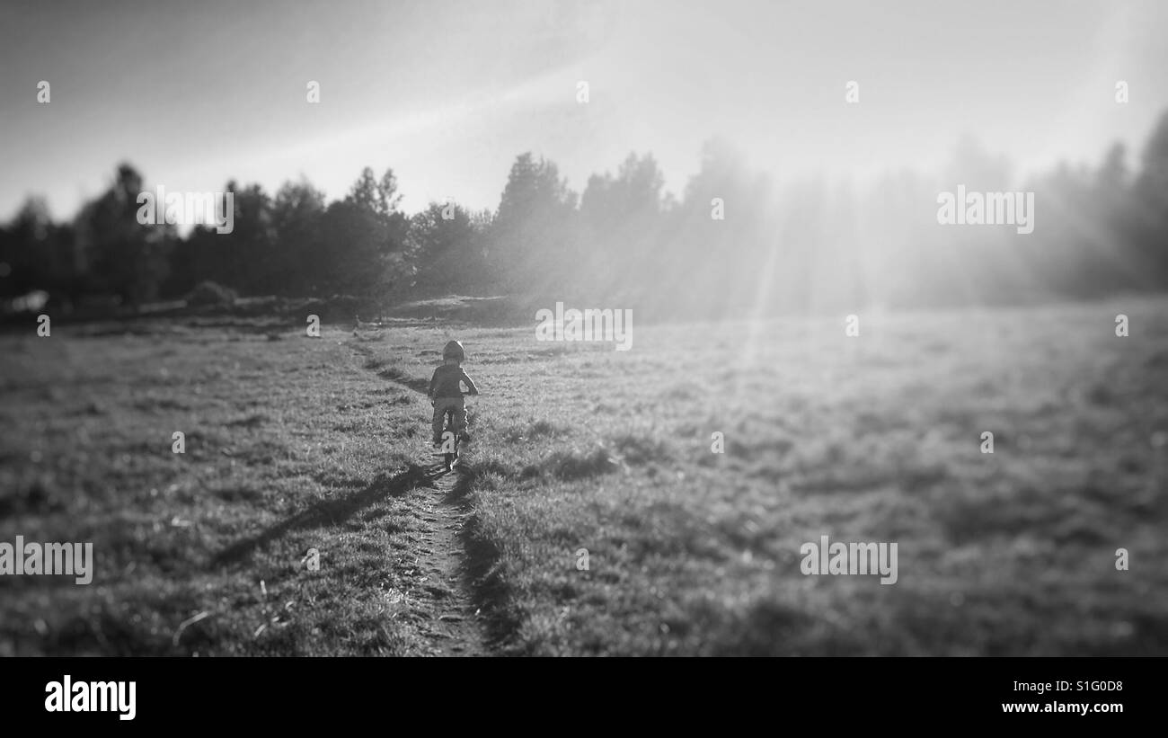 Jeune enfant équitation vélo le long de sentiers à voie unique dans le champ Banque D'Images