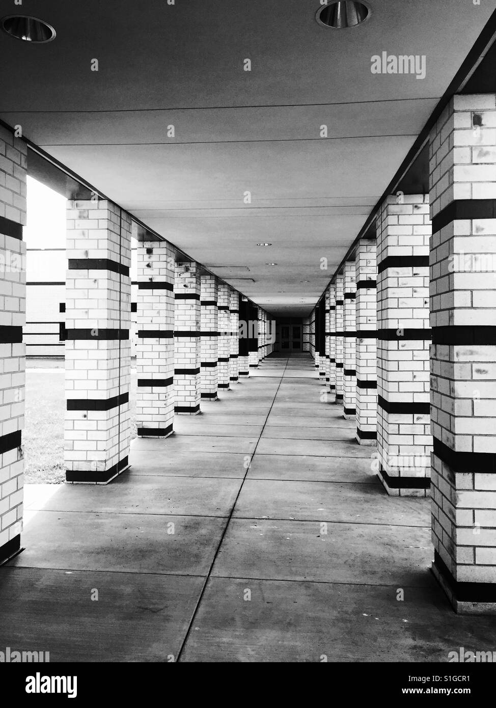 Une image en noir et blanc d'un long passage couvert menant à une porte, flanquée de piliers Banque D'Images