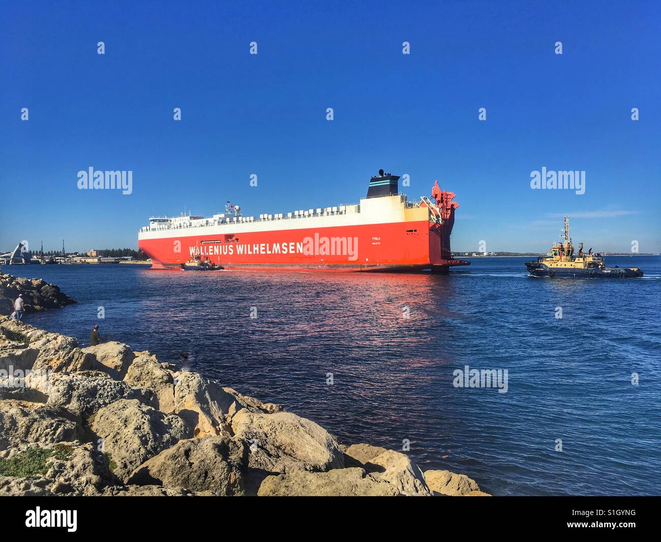 D'énormes porte-conteneurs, l'entrée du port de Fremantle. Deux remorqueurs de diriger le navire jusqu'au port. Les gens pêchent dans l'avant-plan. Banque D'Images