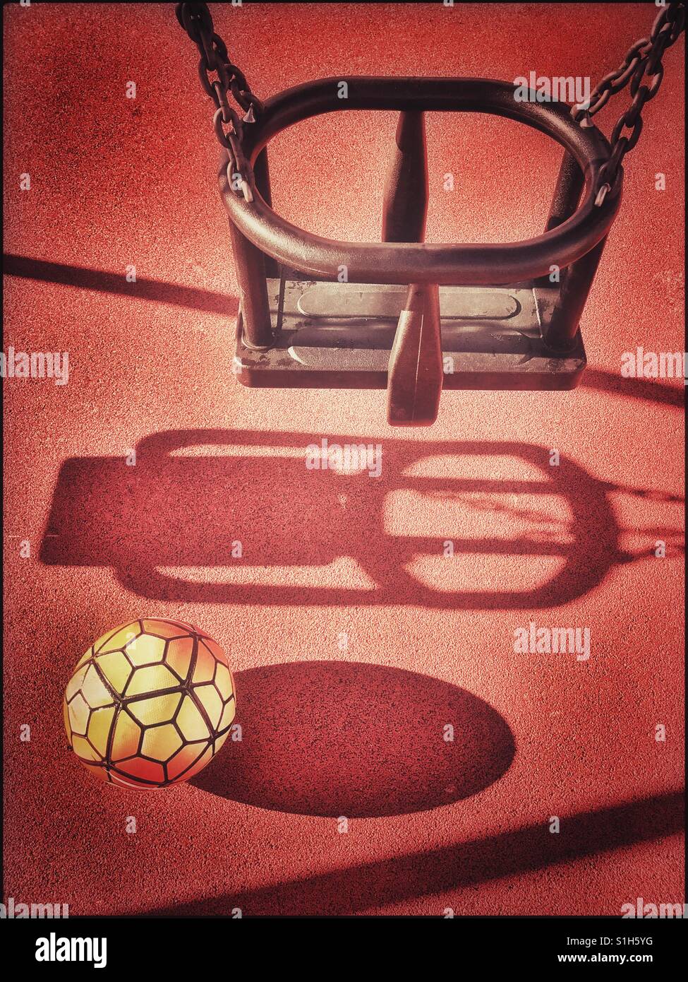 Une famille de football jaune a été abandonné sous une balançoire dans un aire de jeu pour enfants. Il y a des ombres sur le sol. Où sont les enfants ? Photo © COLIN HOSKINS. Banque D'Images