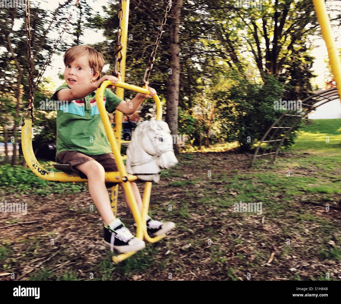 Curieux boy swinging sur vintage cheval à bascule à l'extérieur sur l'ensemble d'oscillation. Banque D'Images