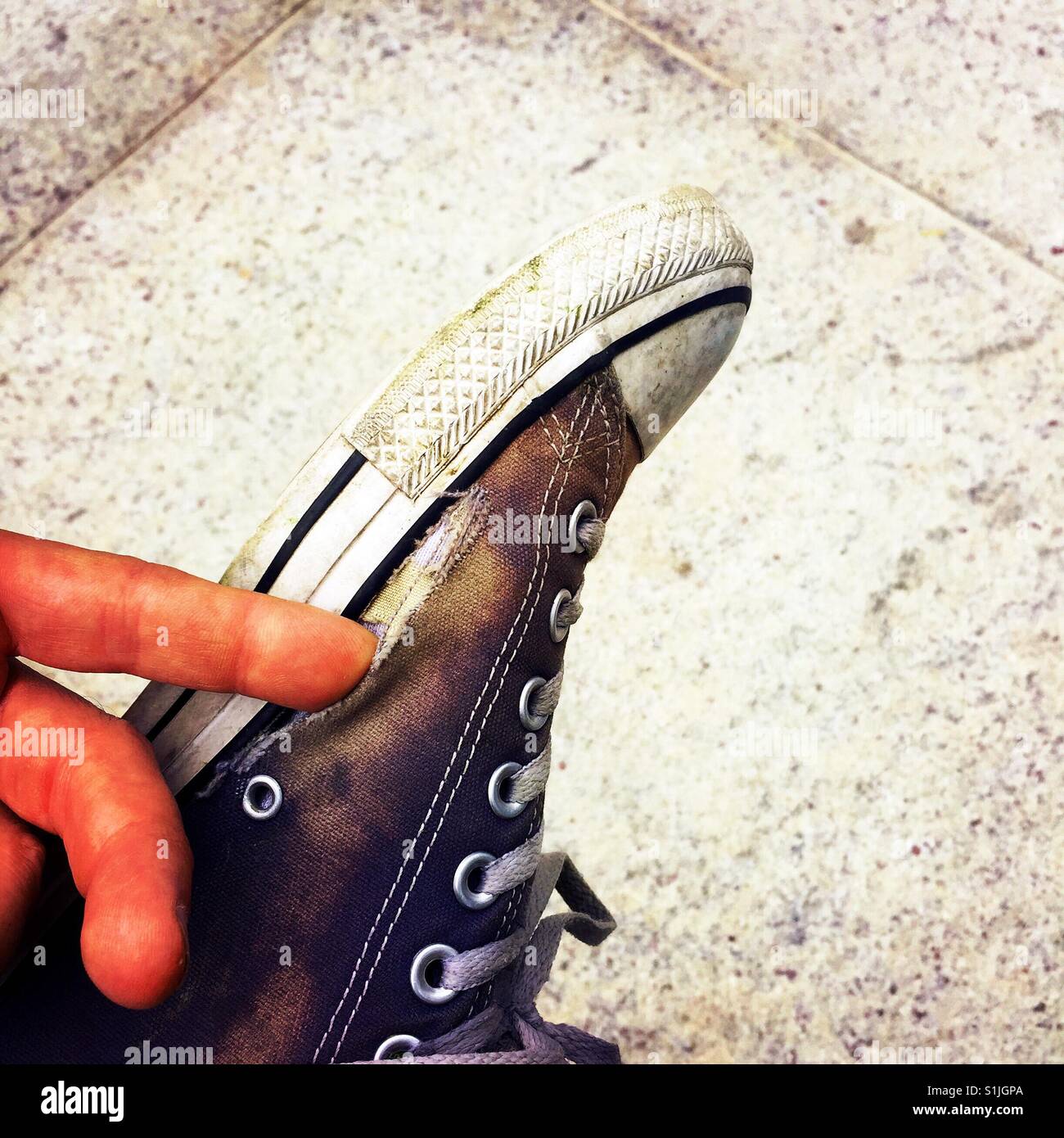 Un homme assis jambes croisées et poussant son doigt dans un trou dans sa  chaussure Converse bien usé Photo Stock - Alamy