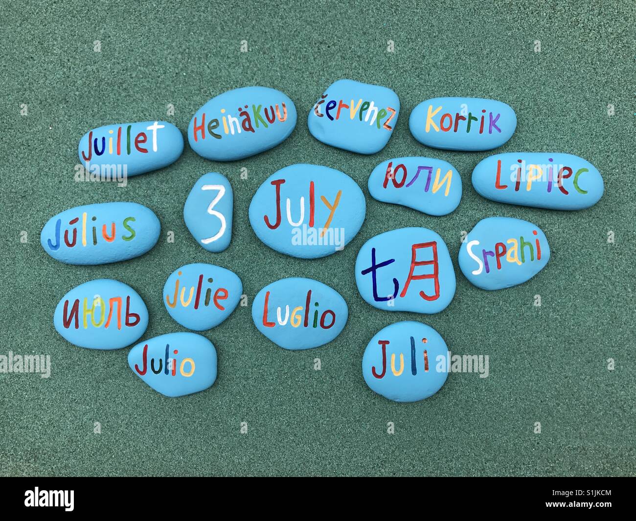 3 juillet, date du calendrier en plusieurs langues sur les pierres de couleur sur le sable vert - Image de stock capturée avec un smartphone