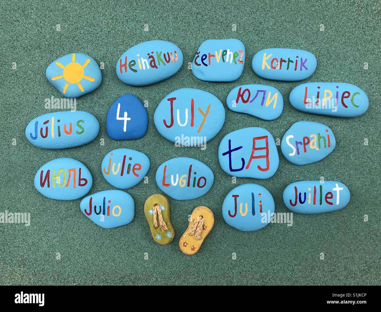 4 juillet, date du calendrier en plusieurs langues sur les pierres de couleur sur le sable vert - Image de stock capturée avec un smartphone