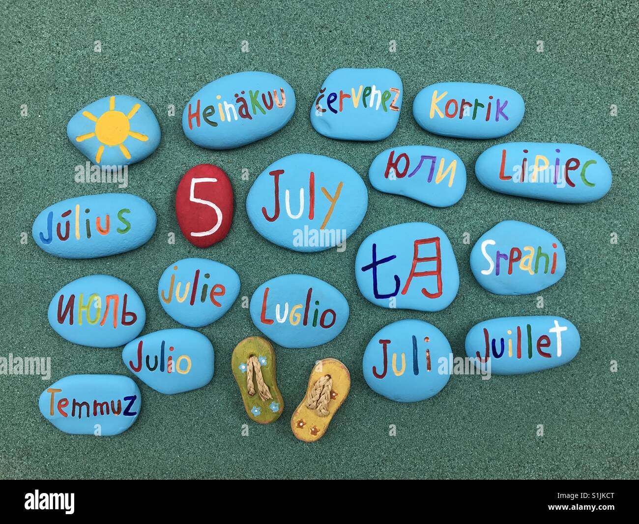 5 juillet, date du calendrier en plusieurs langues sur les pierres de couleur sur le sable vert - Image de stock capturée avec un smartphone