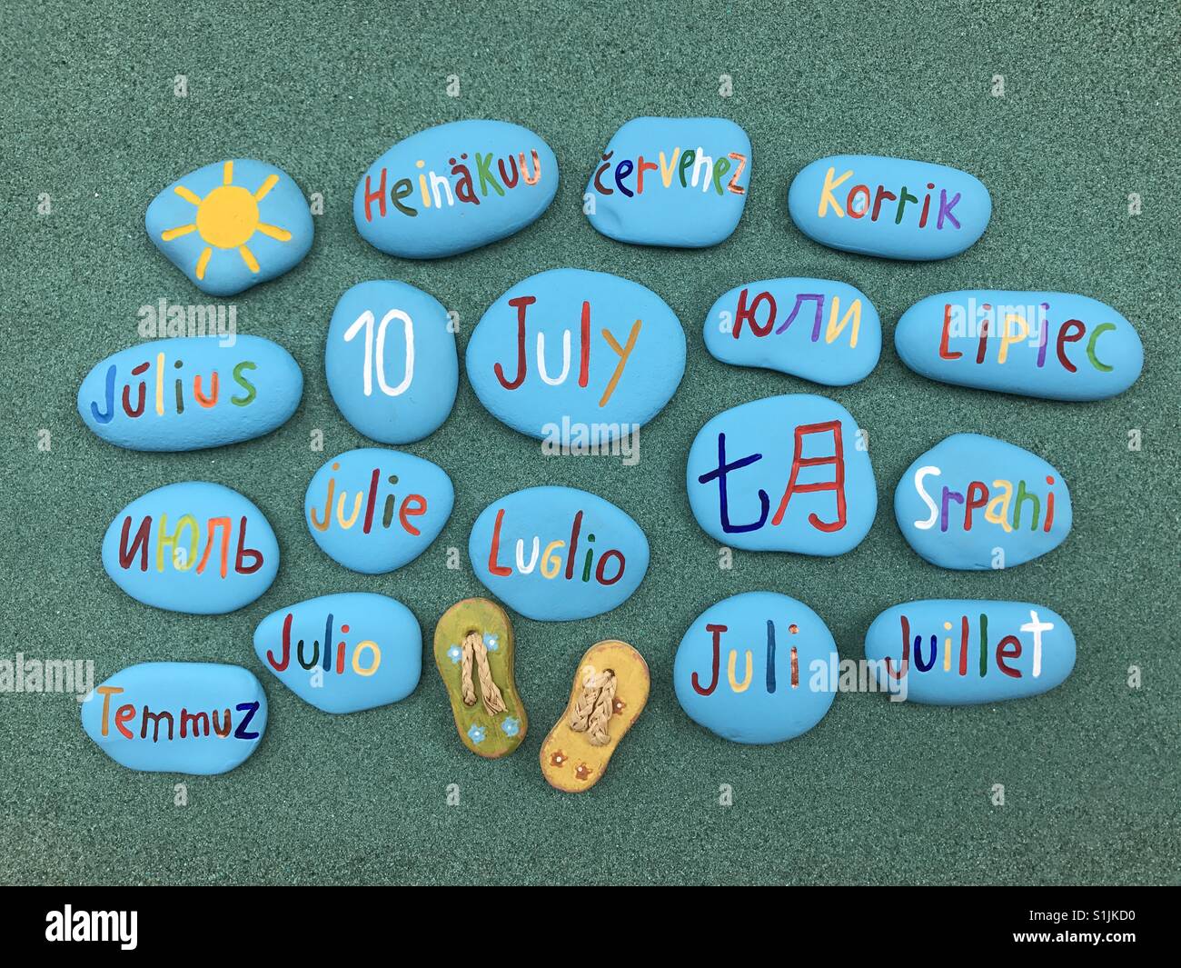 10 juillet, date du calendrier en plusieurs langues sur les pierres de couleur sur le sable vert - Image de stock capturée avec un smartphone