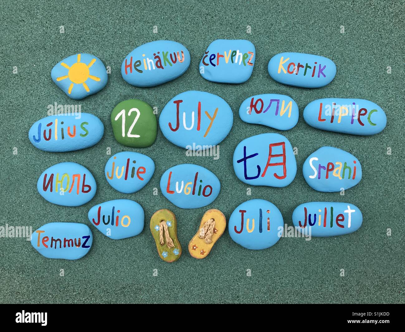 12 juillet, date du calendrier en plusieurs langues sur les pierres de couleur sur le sable vert - Image de stock capturée avec un smartphone