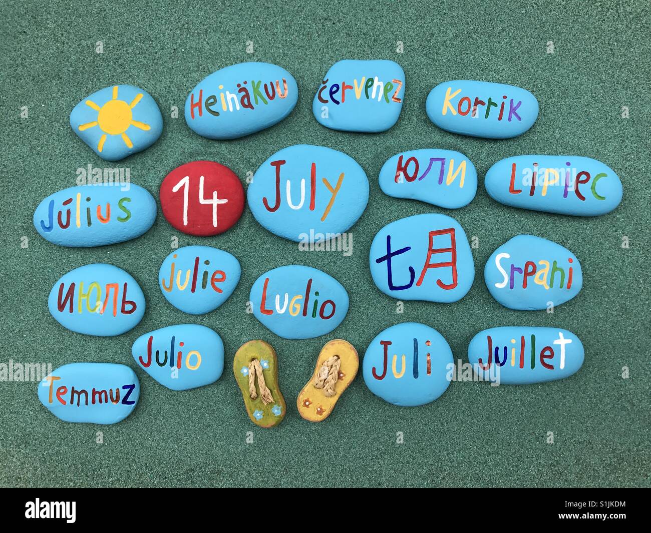14 juillet, date du calendrier en plusieurs langues sur les pierres de couleur sur le sable vert - Image de stock capturée avec un smartphone