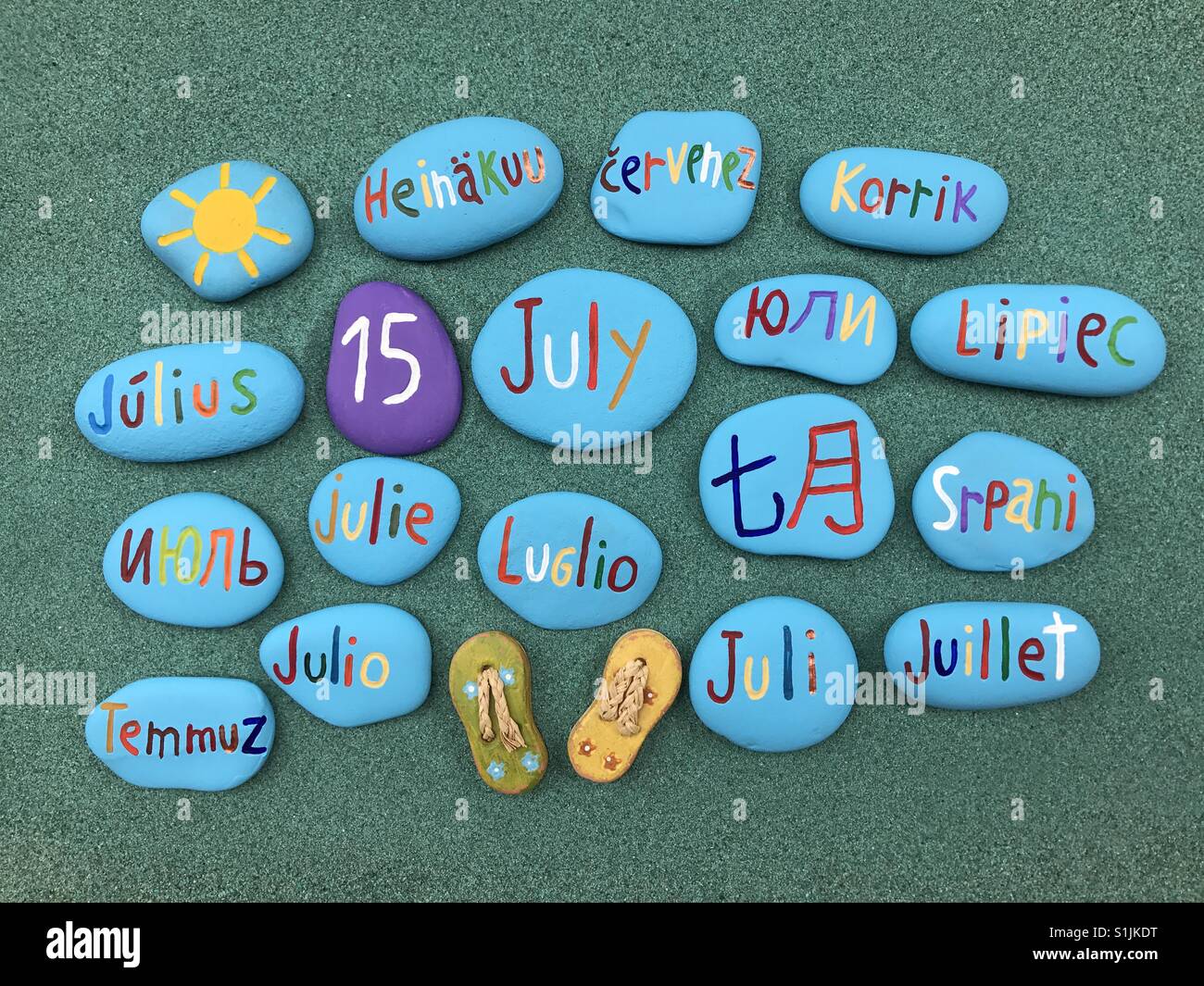 15 juillet, date du calendrier en plusieurs langues sur les pierres de couleur sur le sable vert - Image de stock capturée avec un smartphone