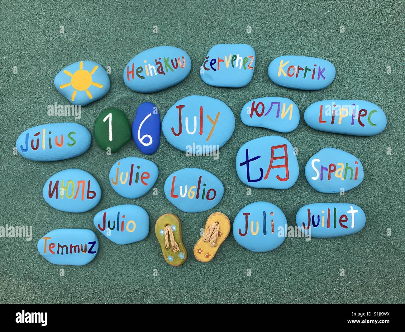 16 juillet, date du calendrier en plusieurs langues sur les pierres de couleur sur le sable vert - Image de stock capturée avec un smartphone