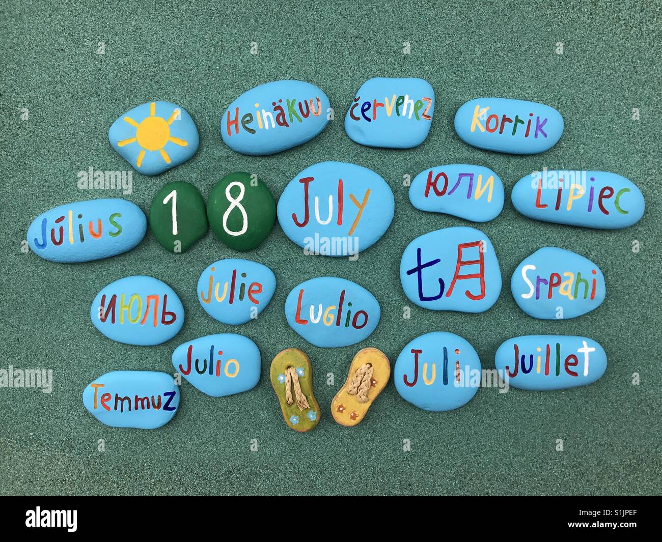 18 juillet, date du calendrier en plusieurs langues sur les pierres de couleur sur le sable vert - Image de stock capturée avec un smartphone