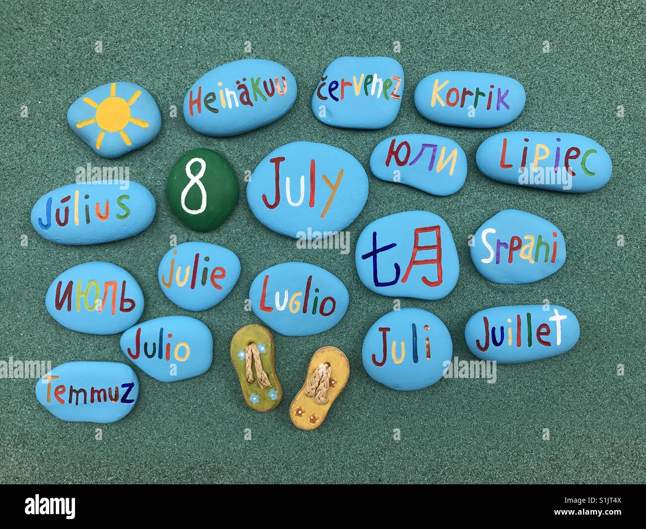 8 juillet, date du calendrier en plusieurs langues sur les pierres de couleur sur le sable vert - Image de stock capturée avec un smartphone