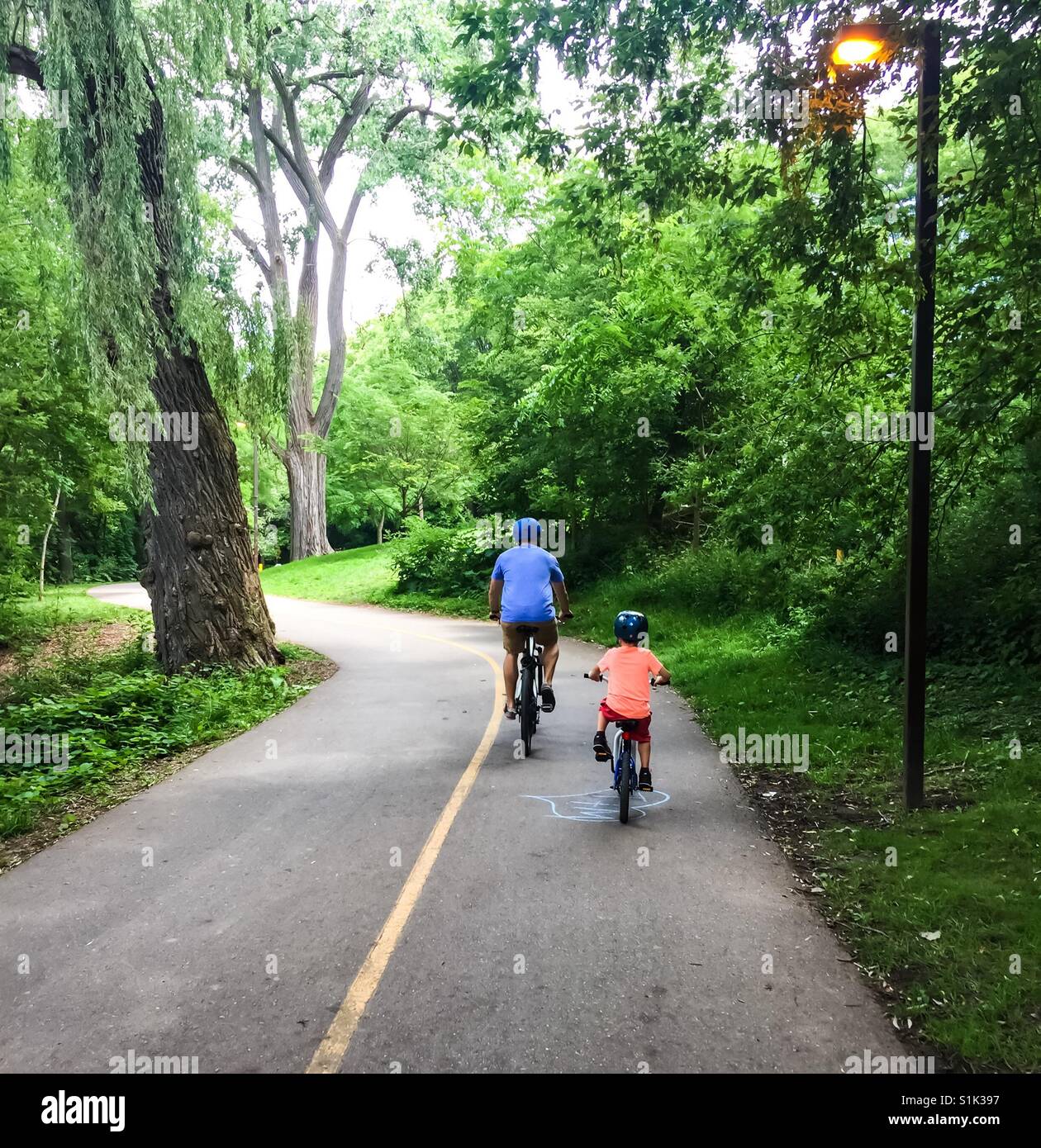 Père et fils à vélo dans un parc, une belle sortie estivale dans un cadre vert et rafraîchissant, Ontario, Canada. Concepts: Ensemble, papa et moi, moi. Facile à conduire. Fête des pères. - Image de stock capturée avec un smartphone