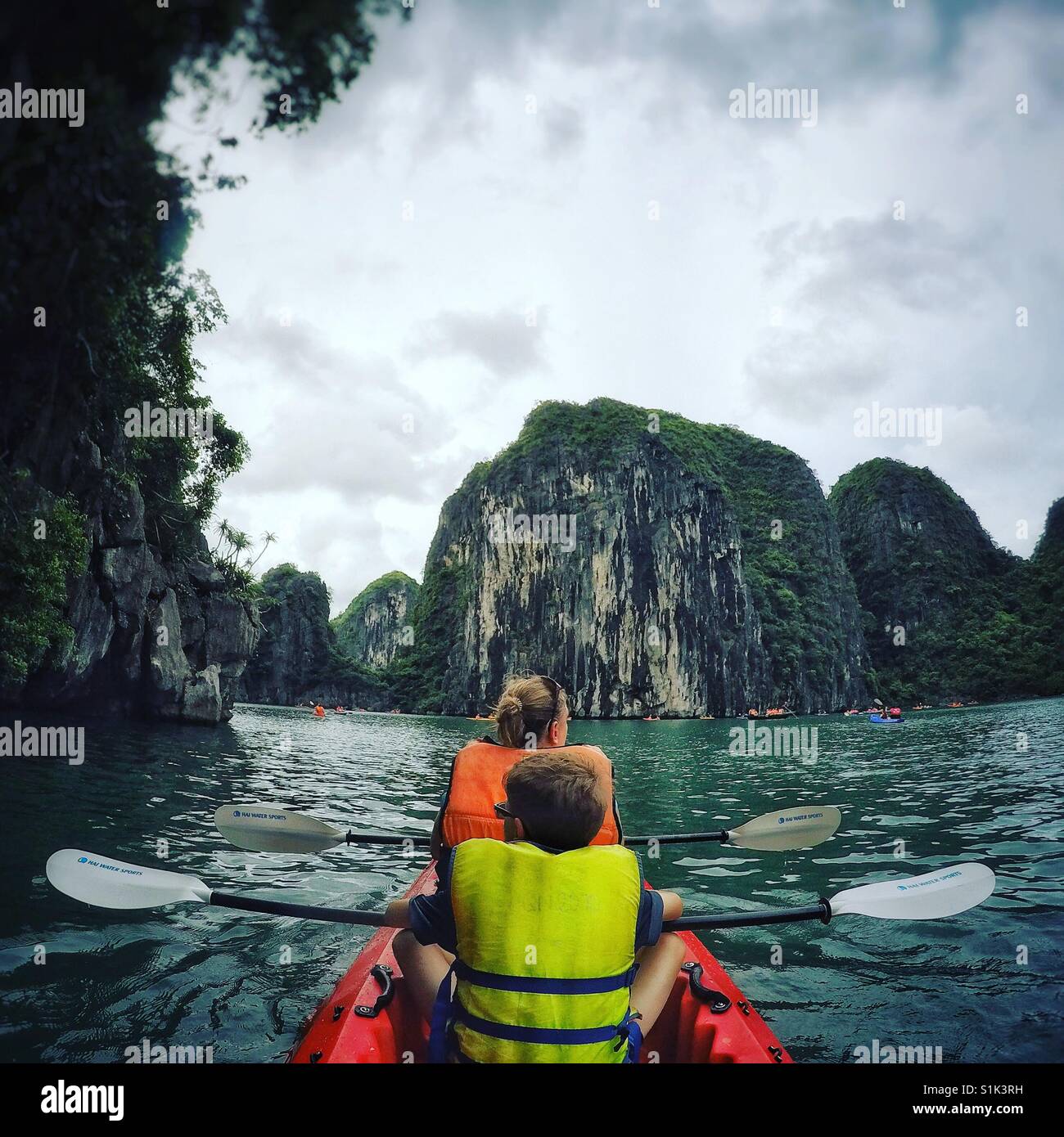 Une famille d'un adulte et enfant kayak dans les eaux émeraude de la Baie d'Halong au Vietnam. Calcaire recouvert de forêt tropicale. Banque D'Images