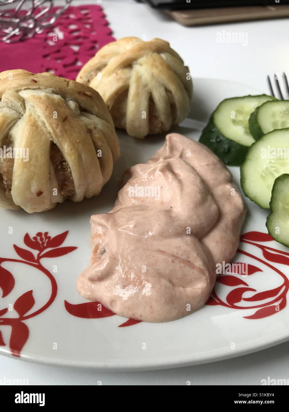 Boulettes de viande hachée cuite au four enveloppé dans des bandes de pâte feuilletée. Des grappes de viandes hachées et de la pâte. Ils se couchaient dans une assiette. Ensuite, ​​Cucumbers en tranches et la sauce. Banque D'Images