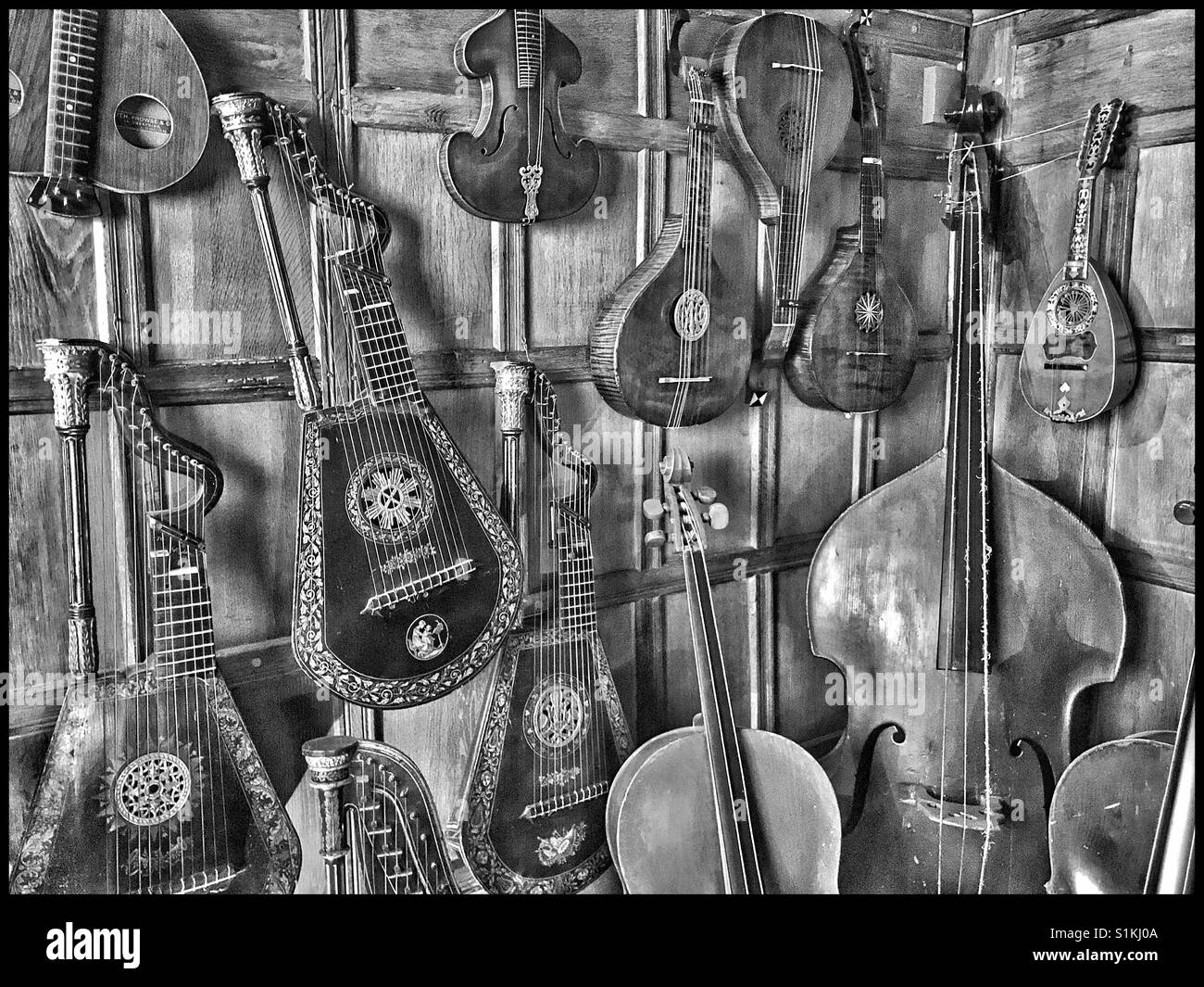 Une image monochrome montrant une collection d'instruments à cordes dans le coin lambrissés d'une maison de campagne. Harpe, violons et guitares sont visibles. Crédits photos - © COLIN HOSKINS. - Image de stock capturée avec un smartphone