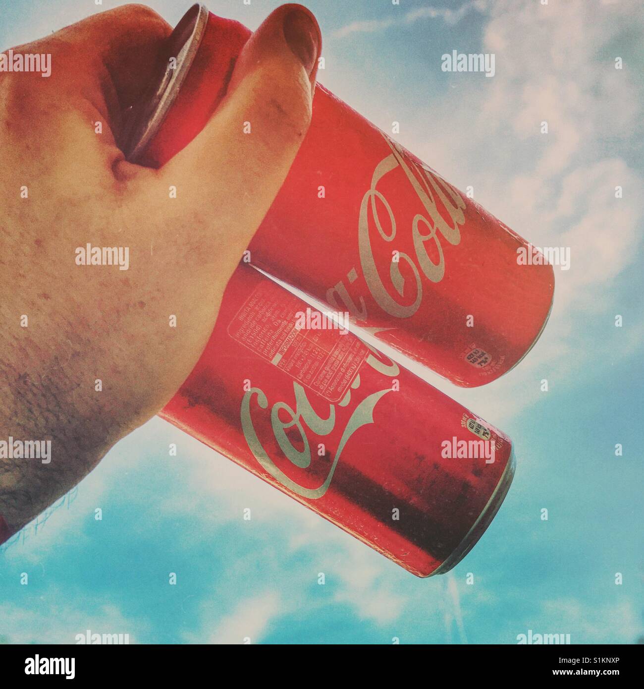 Main humaine avec 2 boîtes de coca-cola sur un ciel ensoleillé Banque D'Images