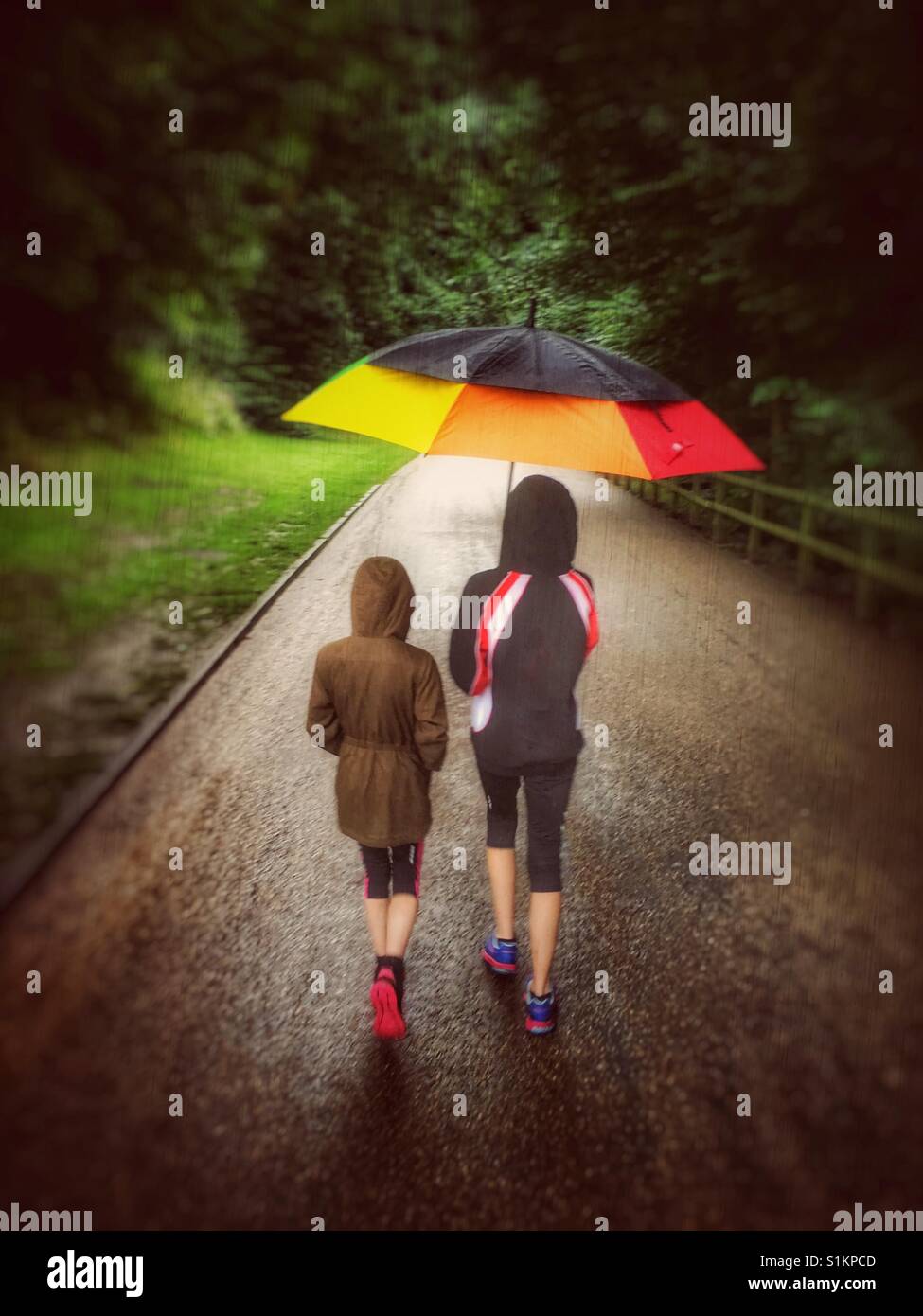 Deux jeunes filles dans le parc sous la pluie sous un grand parapluie coloré Banque D'Images