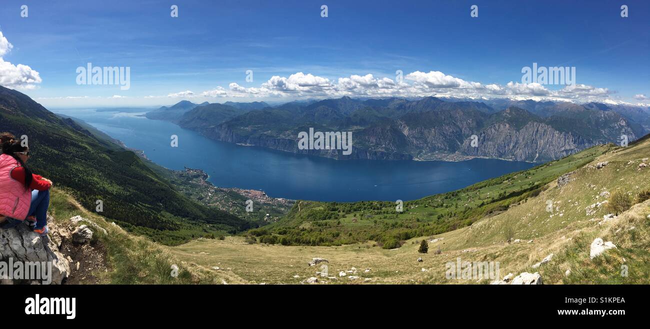 Le lac de Garde, Italie - Mai 2017 : vue panoramique depuis le Monte Baldo à jusqu'à Malcesine avec un visiteur assis sur un rocher Banque D'Images