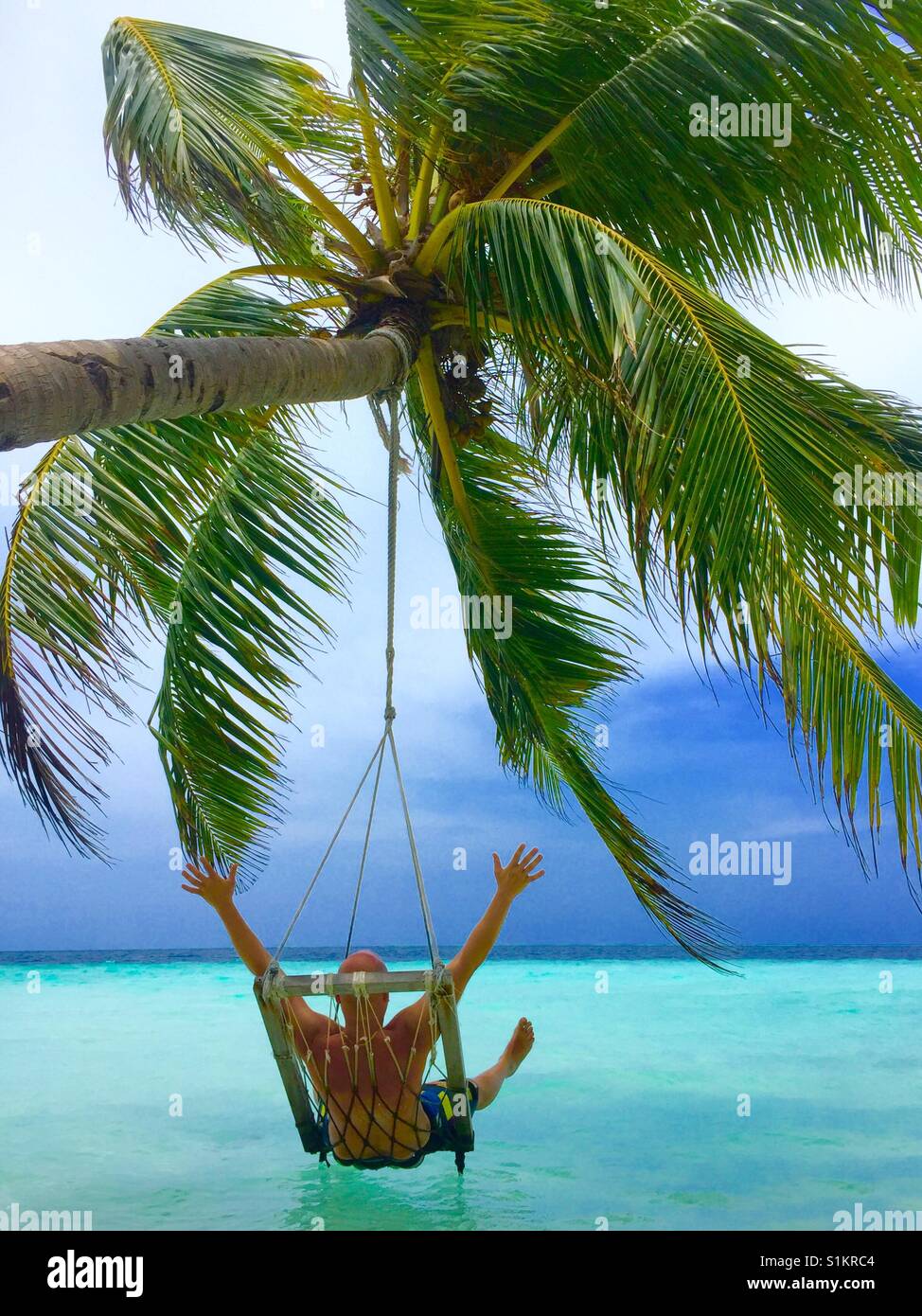 Jeune Homme Profitant De L Instant De La Liberte Et Le Bonheur De La Maison De Vacances Avec Ses Mains En L Air En Swing Suspendu A Cocotier Sur L Eau Claire Dans Les Maldives