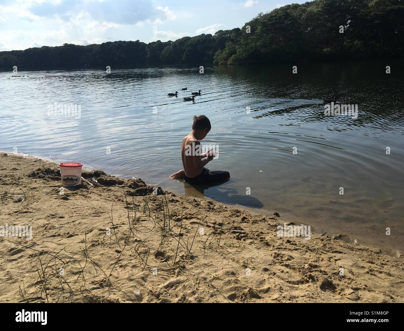 Un garçon dans un lac, les canards en arrière-plan Banque D'Images