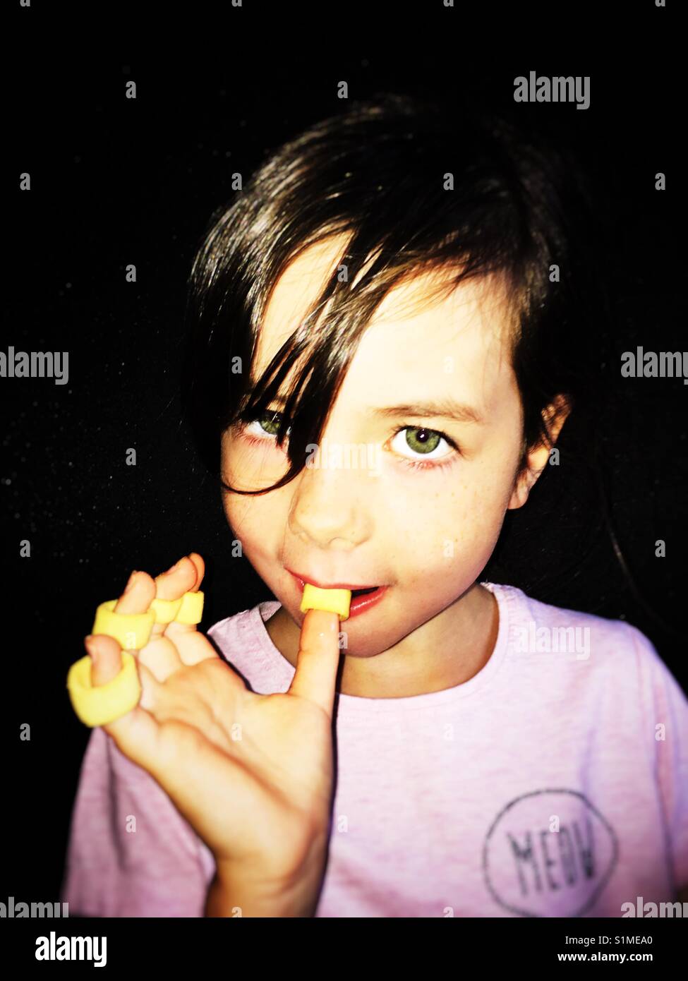 Girl eating Cerceaux anneaux de pommes de terre de ses doigts et les pouces Banque D'Images
