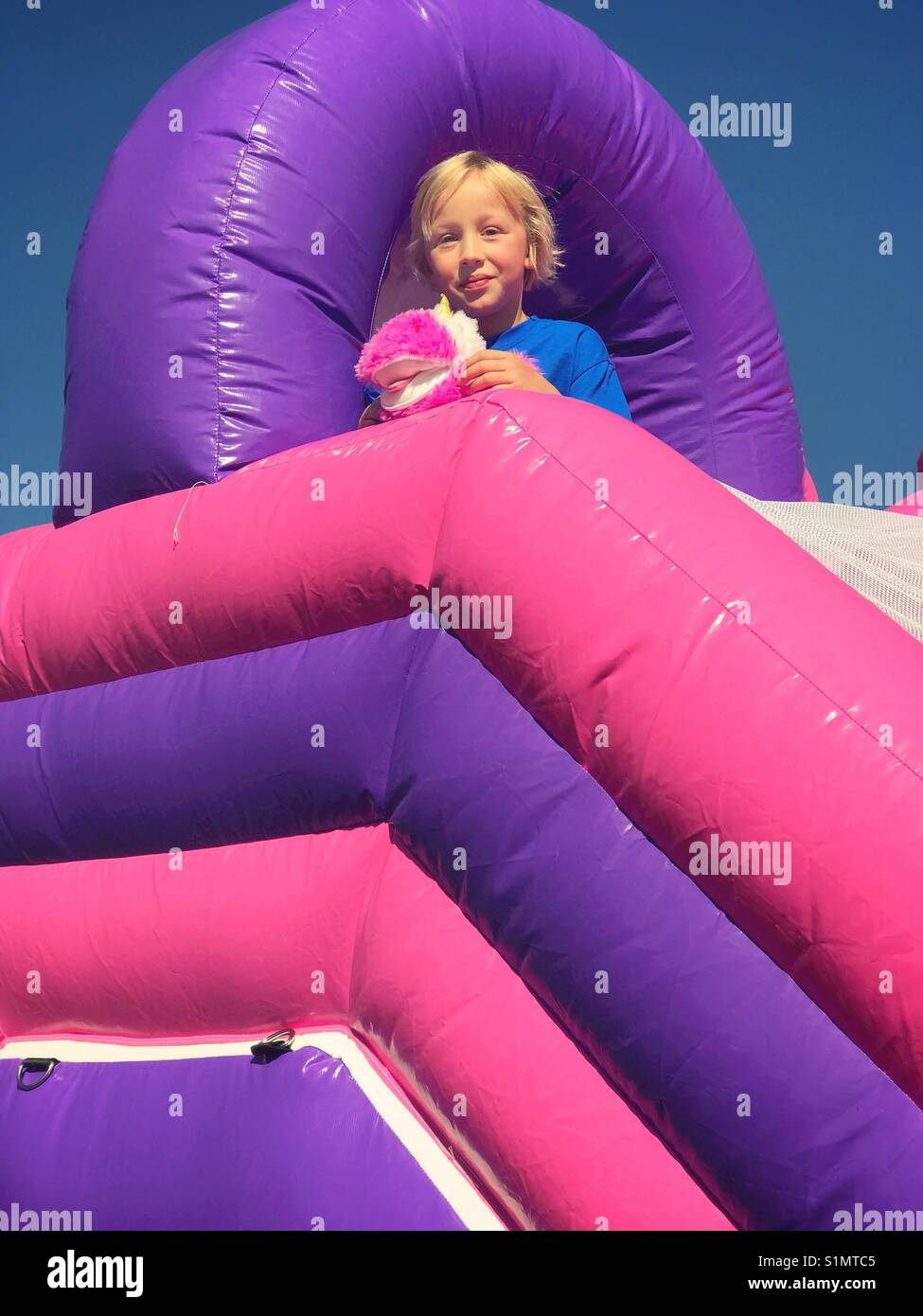Une fille avec une peluche se tient au sommet d'une structure de jeux gonflables. Banque D'Images