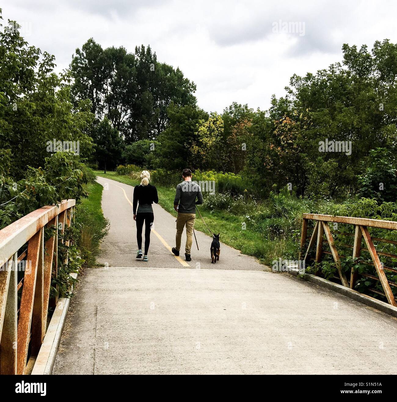 Un jeune couple et un chien sur un chemin à travers des arbustes et des arbres par une chaude journée. Concepts famille, sortie, plein air, loisirs, de stresser, communication avec la nature, air frais - Image de stock capturée avec un smartphone