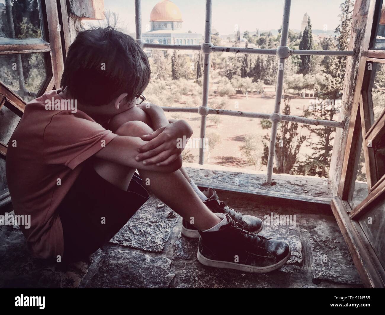Un jeune garçon regarde par la fenêtre, donnant sur une cour arabe, à travers la fenêtre de l'école primaire de Jérusalem. Banque D'Images