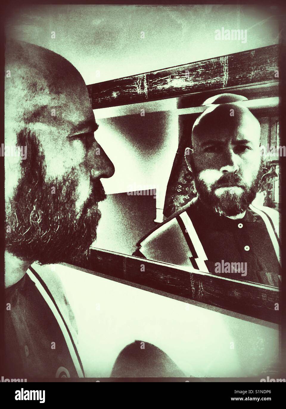Homme chauve barbu à la recherche dans un miroir avec une ombre sur une partie de son visage. Banque D'Images