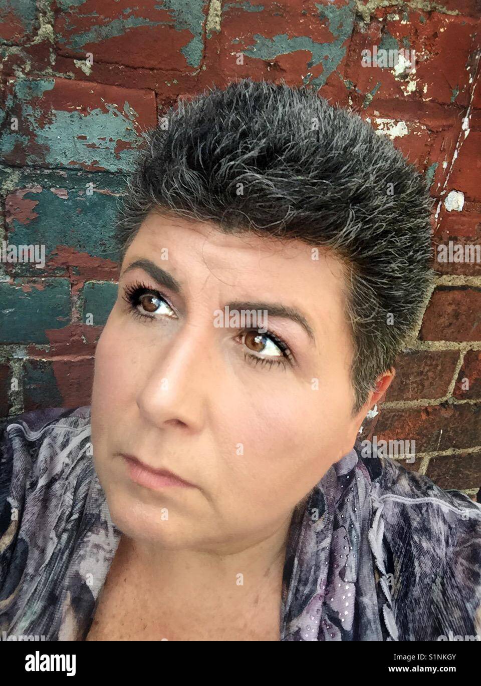 Portrait d'une femme caucasienne d'âge moyen aux cheveux sombres contre un mur de briques Banque D'Images