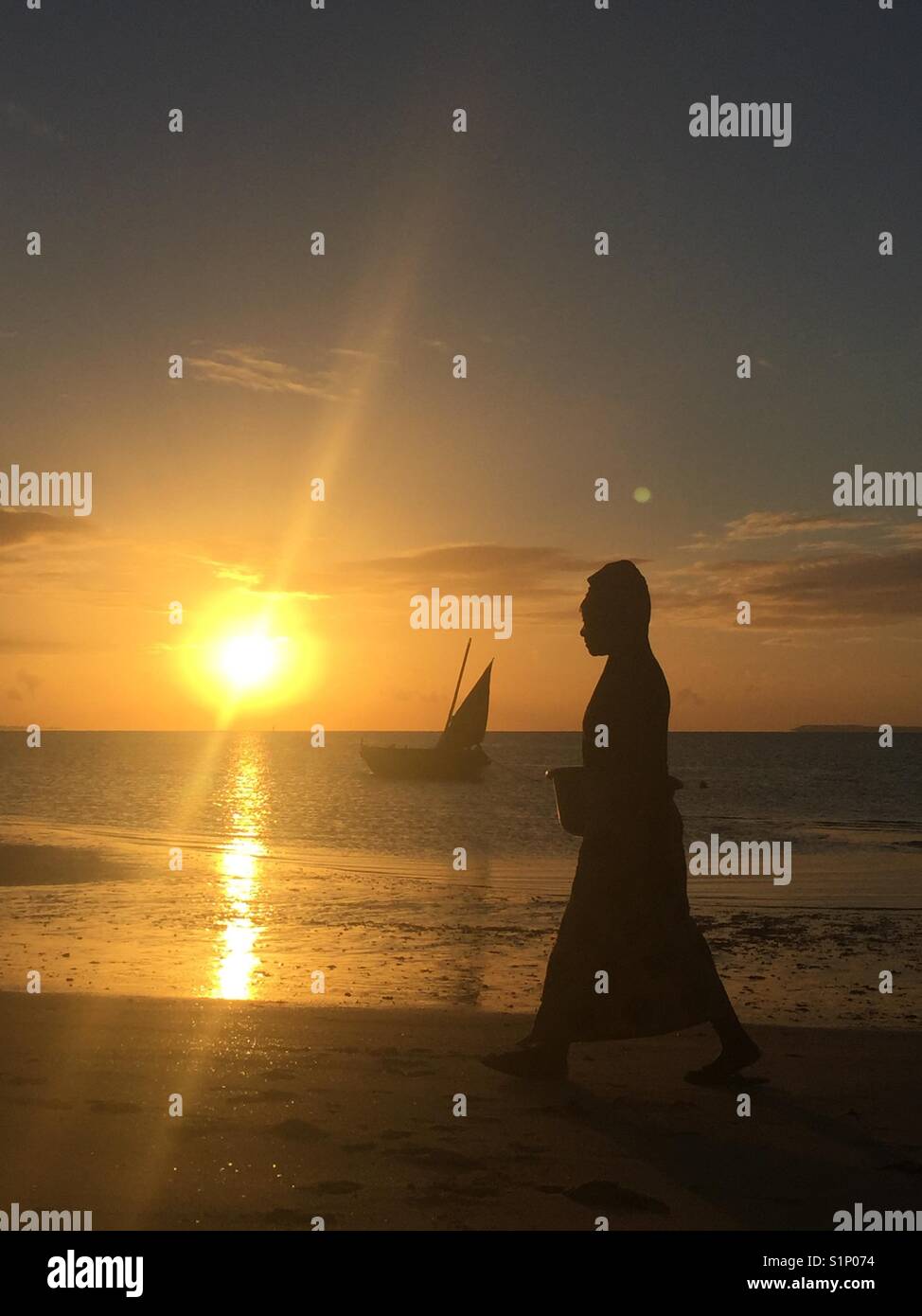 Silhouette de femme africaine au travail à pied au lever du soleil avec un boutre de pêche dans l'arrière-plan. prises au Mozambique Banque D'Images