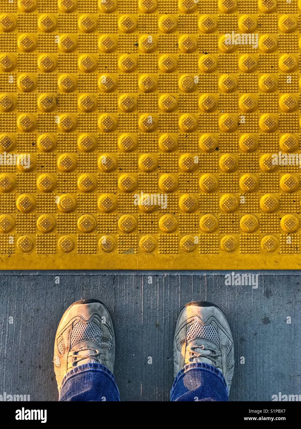 Les pieds d'une personne debout derrière la ligne jaune à une gare. Banque D'Images