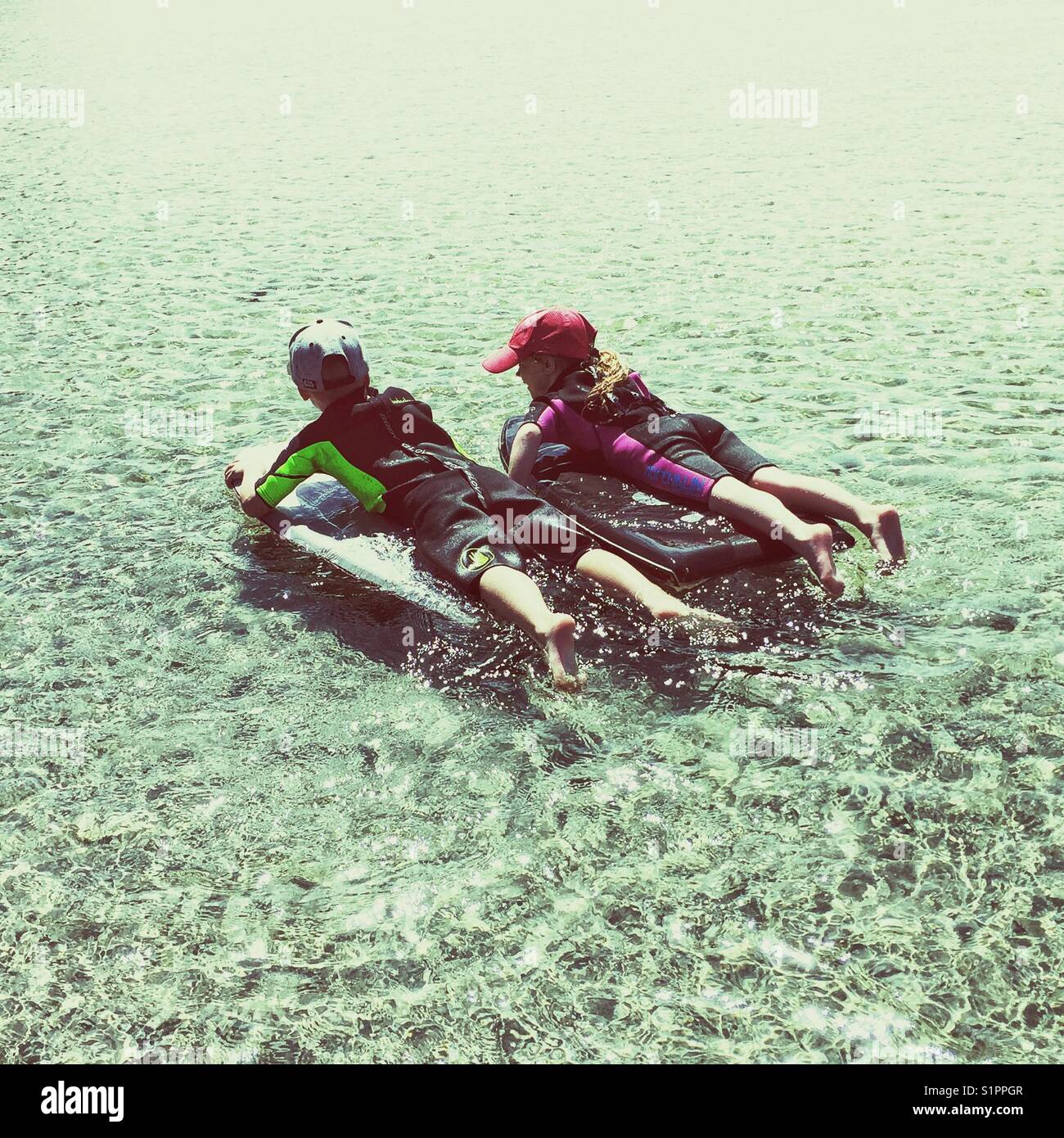 Garçon et fille qui pond sur des planches de corps flottant dans l'eau à la  plage. Enfants portant des combinaisons s'amusant à se détendre sur les  planches de bogie. Liaison frère et