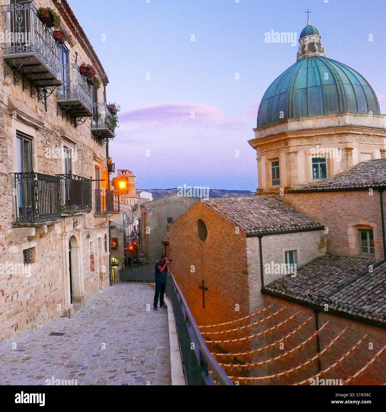 Marche à travers les rues étroites de l'ancien village sicilien de Gangi, avec le dôme de la Cathédrale sur la droite, illuminé par les couleurs du coucher de soleil. Gangi, Palerme, Sicile. L'Italie. Banque D'Images