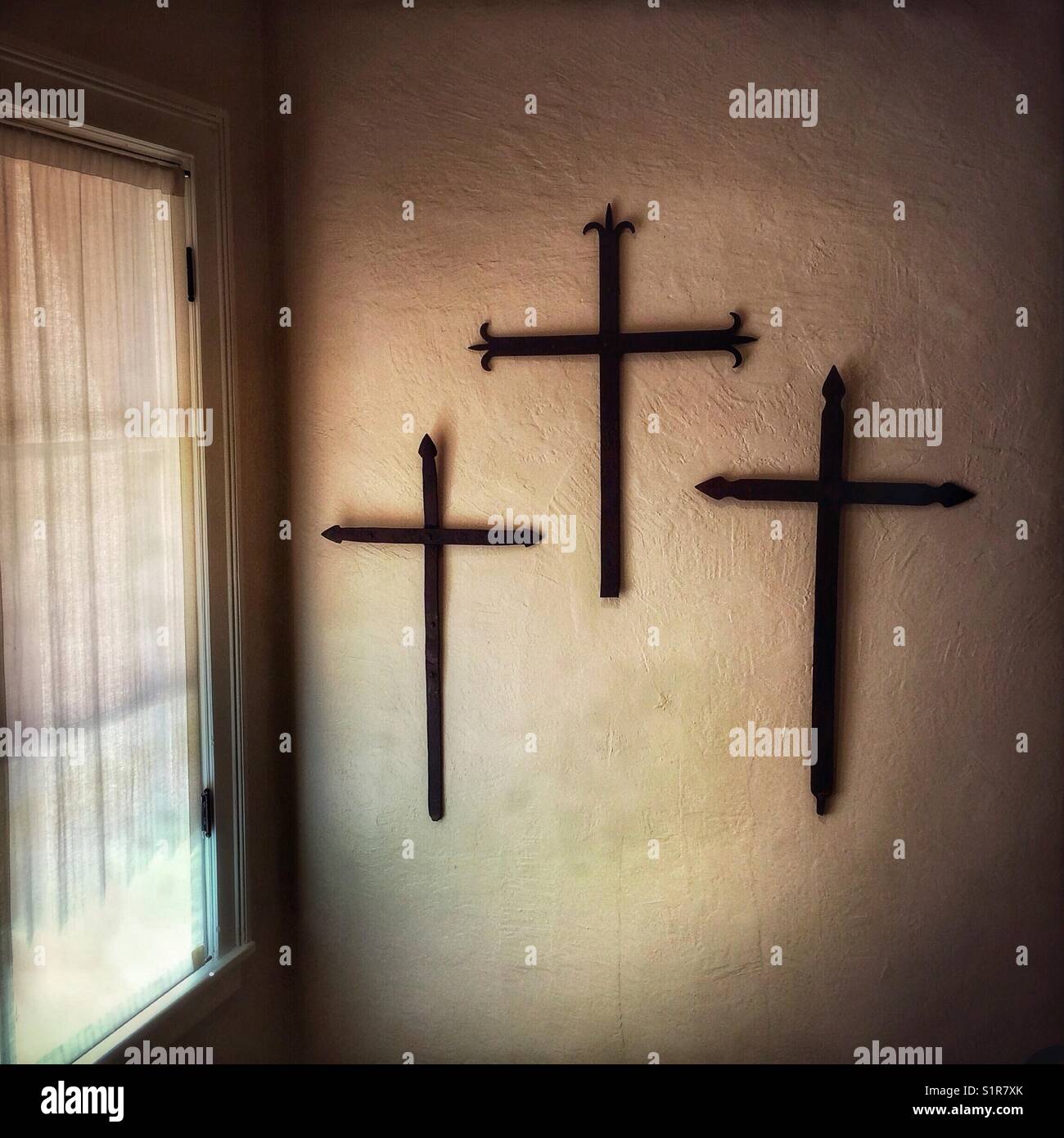 Trois grandes croix de fer accrocher au mur à côté d'une fenêtre avec un rideau de dentelle à Santa Fe, Nouveau Mexique, USA. - Image de stock capturée avec un smartphone