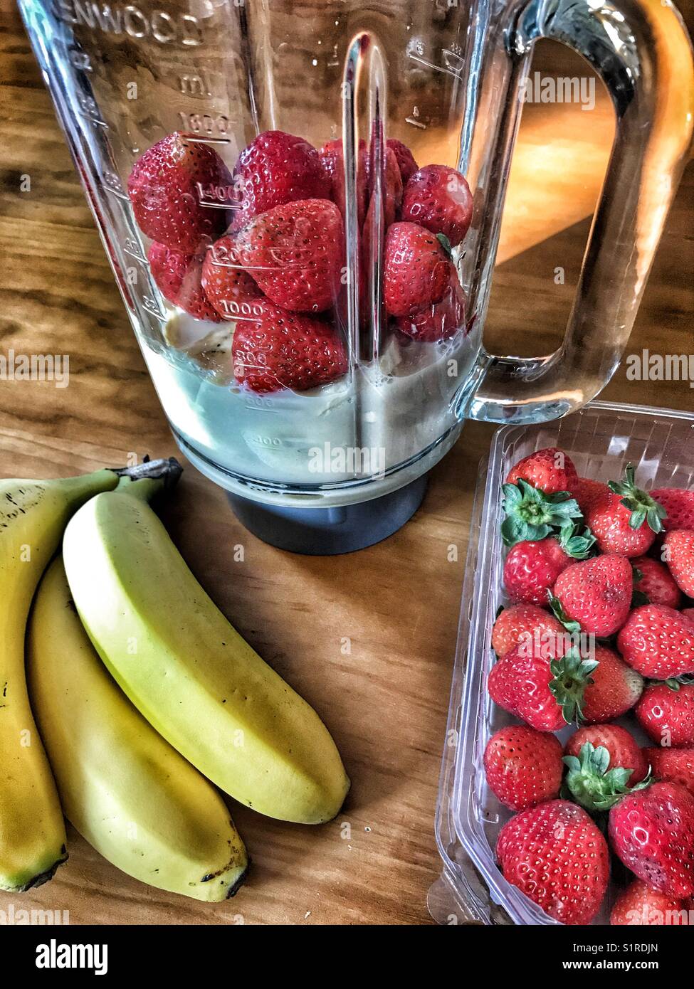 Ingrédients pour préparer un smoothie maison à la fraise, à la banane et au yaourt dans un bol mélangeur en verre - Image de stock capturée avec un smartphone