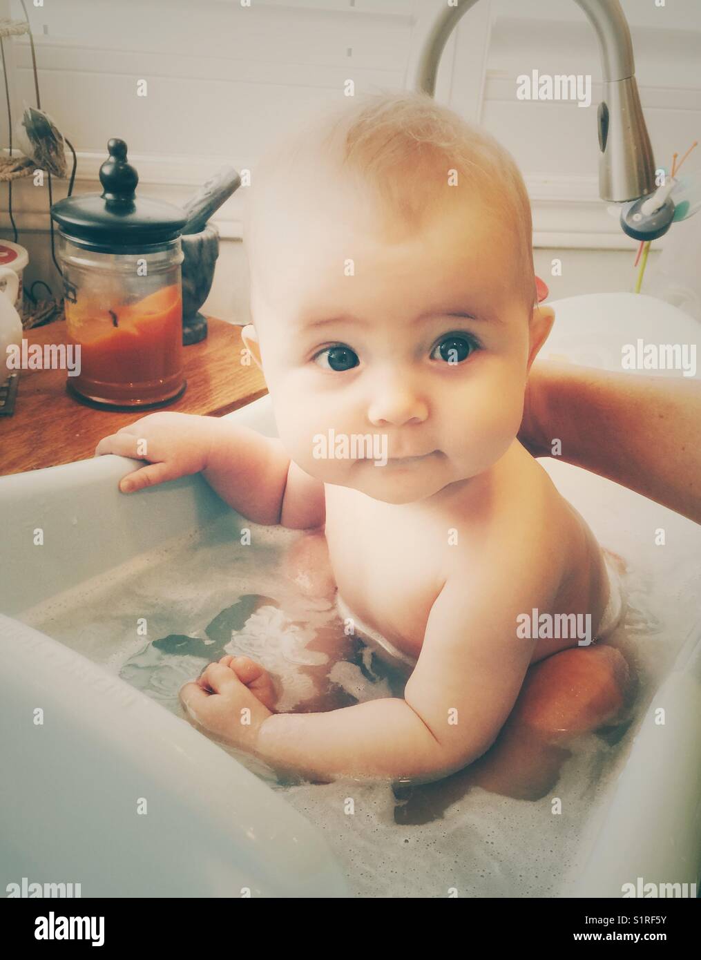Jeune bébé ayant un bain à bulles dans un bébé à remous inséré dans un évier de cuisine Banque D'Images